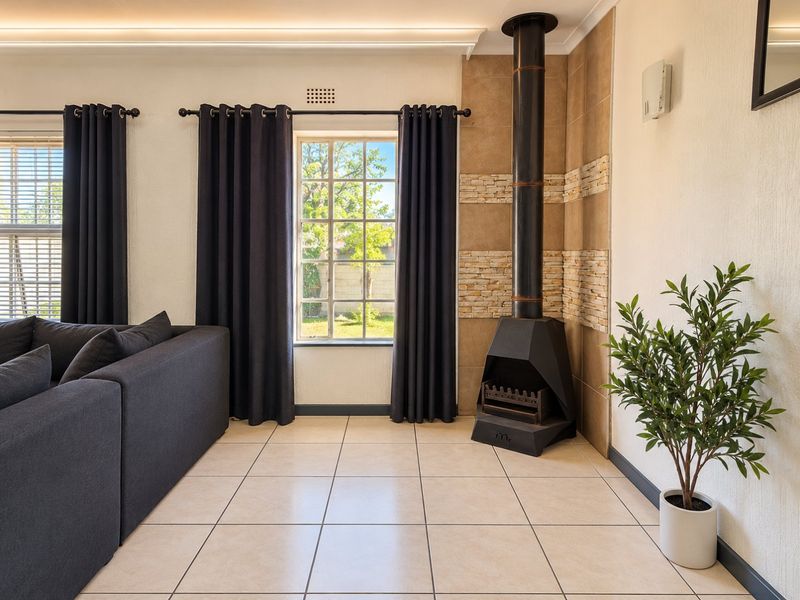 A bright living room featuring tiled flooring, a modern freestanding fireplace with stone cladding, and recessed ceiling lighting.