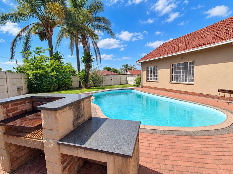 Outdoor entertainment area featuring a swimming pool, brick-paved patio, and a built-in braai, set within a private garden with established palm trees.