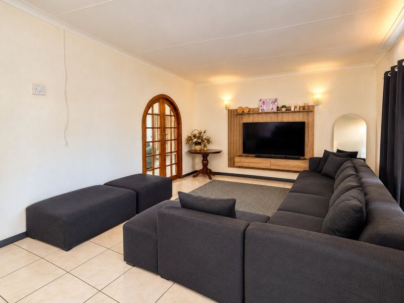 A comfortable living room featuring tiled floors, a built-in media unit, and an elegant arched wooden door leading to adjacent spaces.