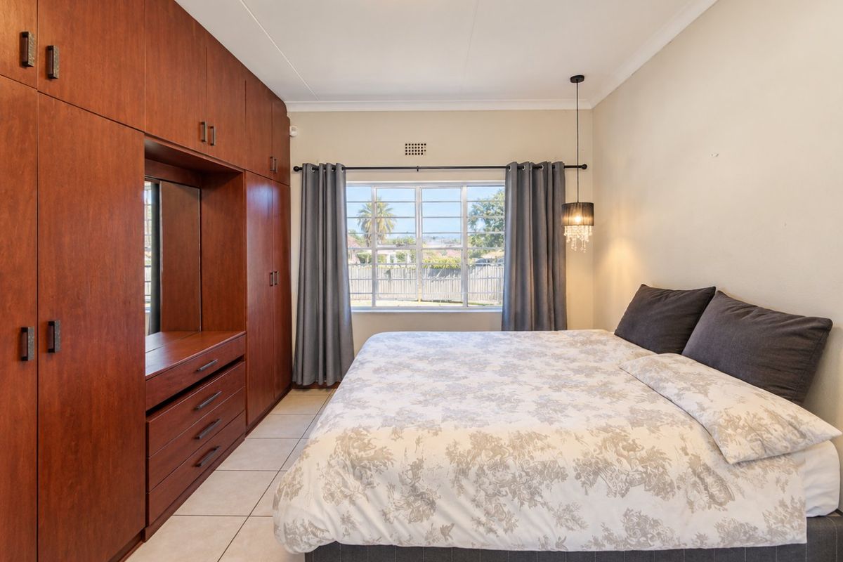 A well-maintained bedroom featuring extensive built-in wooden cabinetry, tiled flooring, and a window with security bars.