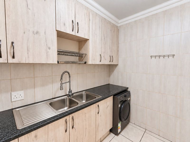 Functional laundry room featuring light wood-grain cabinetry, a double stainless steel sink with a modern faucet, and durable tiled finishes.