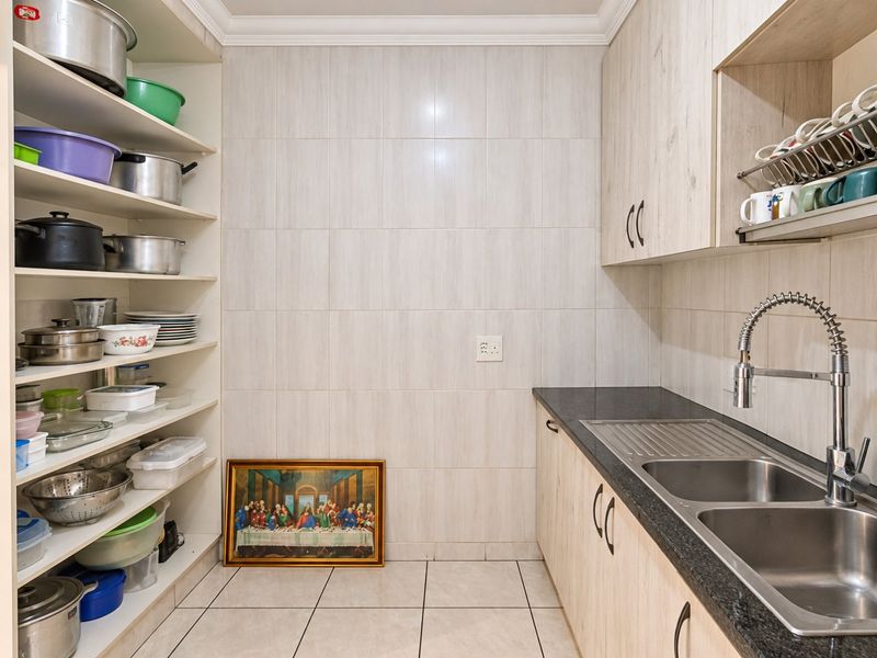 A functional scullery featuring light wood-grain cabinetry, granite countertops, a double stainless steel sink with a gooseneck mixer, and extensive open shelving for storage.