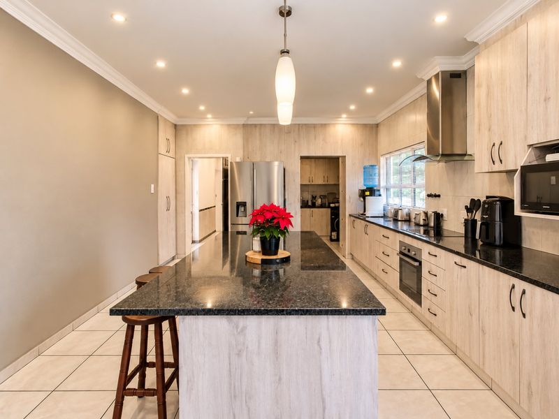 Modern kitchen featuring a large granite-topped island, light wood-grain cabinetry, built-in oven, extractor fan, and recessed lighting with tiled floors.