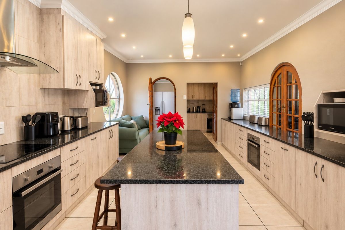 Spacious kitchen featuring a large central island with granite countertops, light wood cabinetry, built-in oven, and modern recessed lighting.