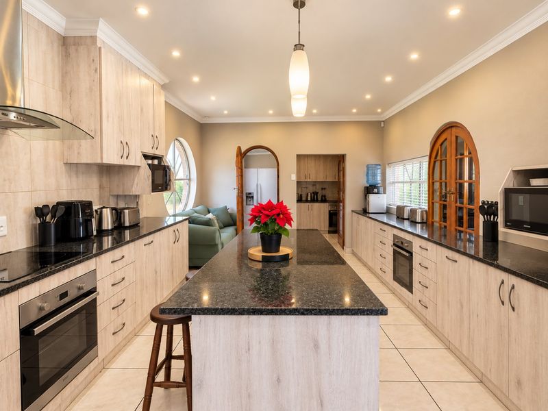 Spacious kitchen featuring a large central island with granite countertops, light wood cabinetry, built-in oven, and modern recessed lighting.