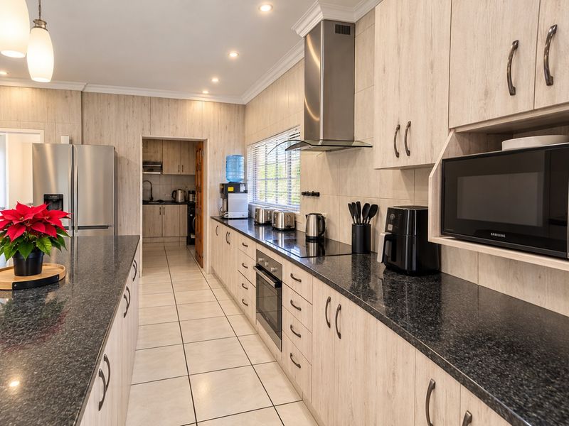 Modern kitchen featuring light wood-grain cabinetry, dark granite countertops, built-in appliances, and a tiled floor, with an adjacent scullery area.