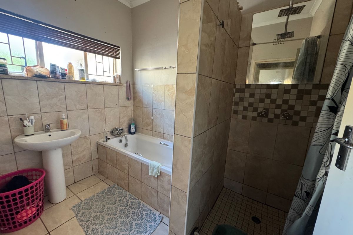 A functional bathroom featuring a pedestal basin, a built-in bathtub, and a separate shower enclosure with tiled finishes throughout.