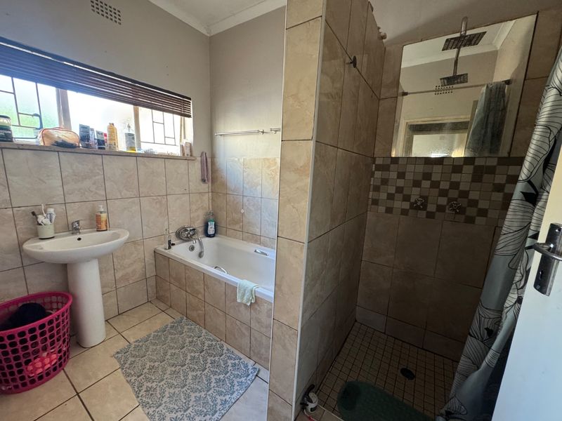 A functional bathroom featuring a pedestal basin, a built-in bathtub, and a separate shower enclosure with tiled finishes throughout.