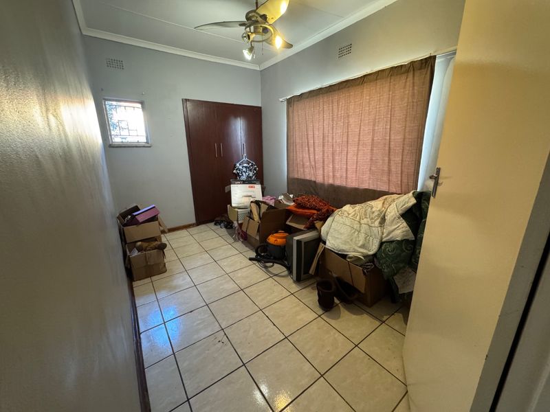 A bedroom featuring tiled flooring, built-in cupboards, and a ceiling fan, offering a functional space ready for personalization.