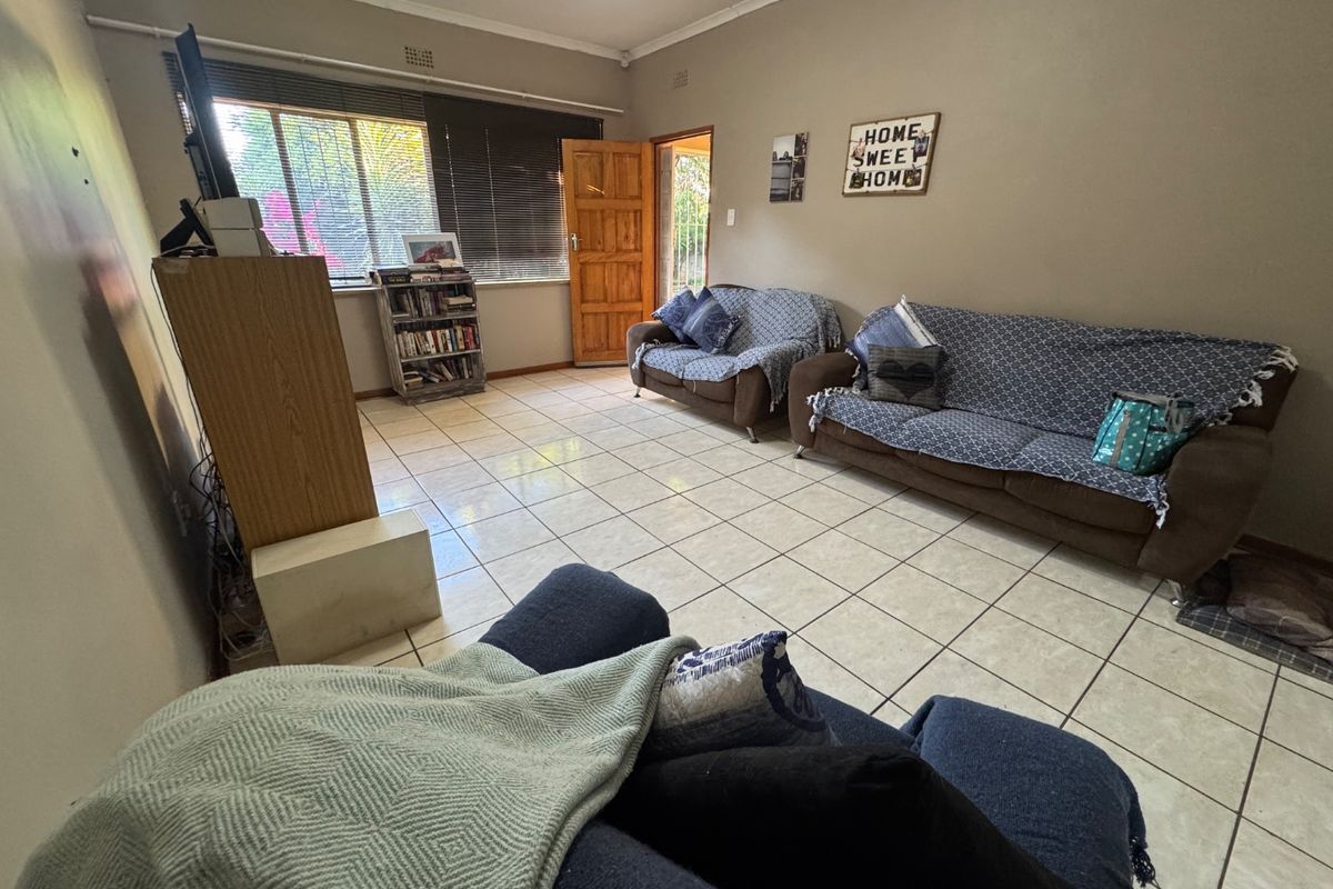 A living room featuring tiled flooring, a timber door, and window blinds, offering a functional space with neutral wall tones.