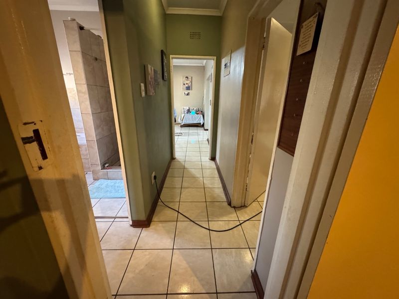 A functional hallway featuring tiled flooring and access to adjacent rooms, including a bathroom, with neutral wall finishes.