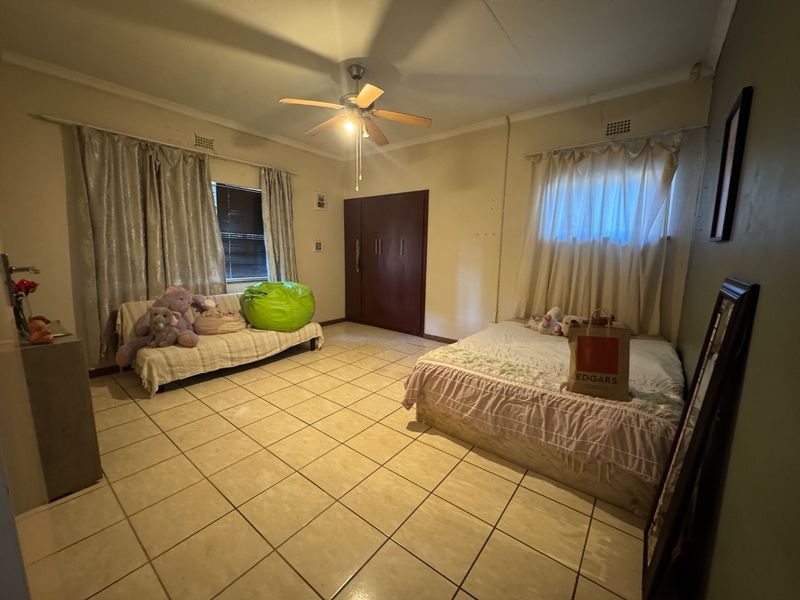 Spacious bedroom featuring tiled flooring, built-in cupboards, and a ceiling fan, offering a functional layout ready for cosmetic updates.