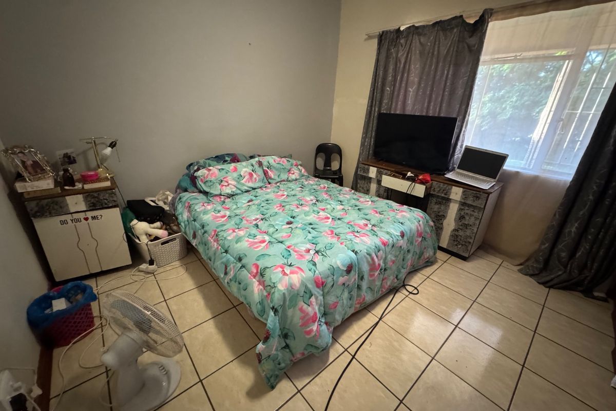 A bedroom featuring tiled flooring and a window with security bars, requiring cosmetic updates to improve the overall aesthetic and condition.