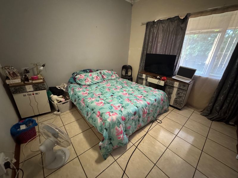 A bedroom featuring tiled flooring and a window with security bars, requiring cosmetic updates to improve the overall aesthetic and condition.