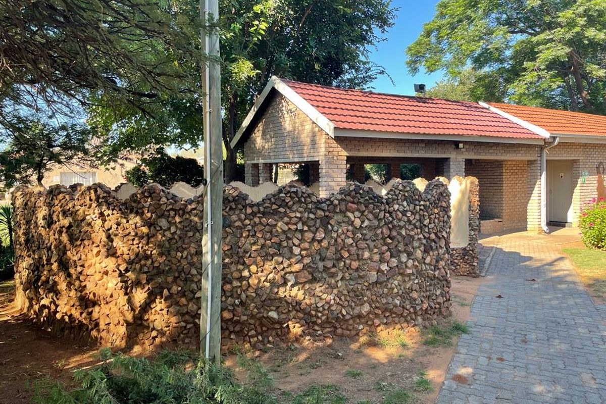 A view of the rear exterior featuring a decorative stone-clad wall, brick structure with a tiled roof, and a paved walkway.