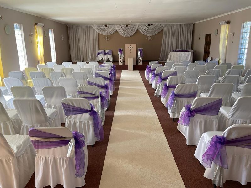 A spacious event hall or clubhouse featuring glass block windows, neutral wall finishes, and carpeted flooring, currently set up for a formal gathering.