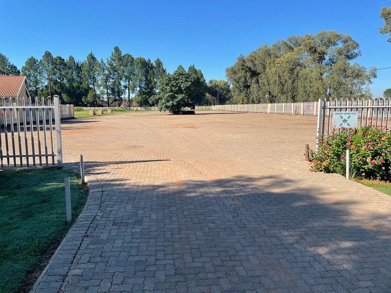 A spacious paved driveway and parking area enclosed by perimeter fencing, featuring a well-maintained garden bed and clear access.
