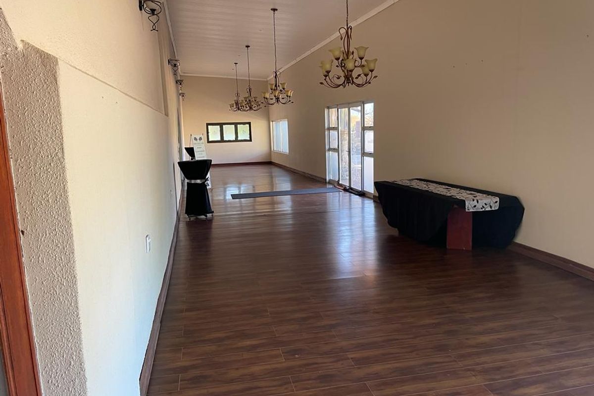 A spacious, elongated living area featuring dark laminate flooring, multiple wrought iron chandeliers, and glass sliding doors providing access to the exterior.