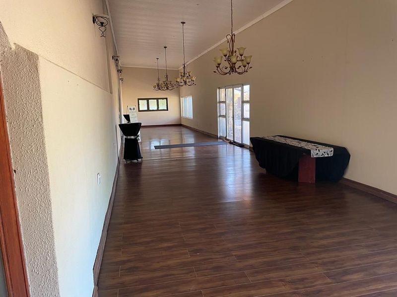 A spacious, elongated living area featuring dark laminate flooring, multiple wrought iron chandeliers, and glass sliding doors providing access to the exterior.