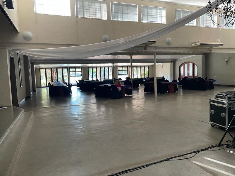 A spacious, open-plan event hall featuring polished concrete floors, high ceilings with abundant natural light, and a raised stage area suitable for various functions.