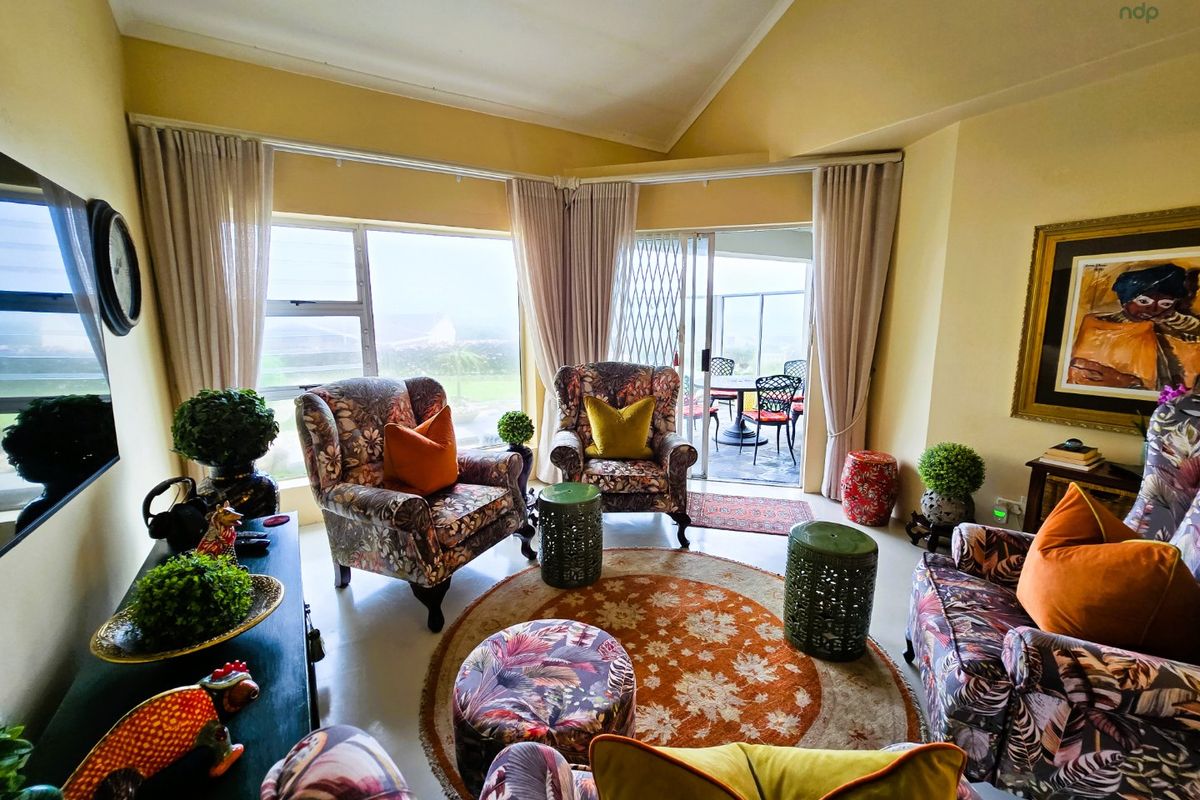 A bright living room featuring a vaulted ceiling, tiled flooring, and large sliding glass doors that provide access to an outdoor patio area.