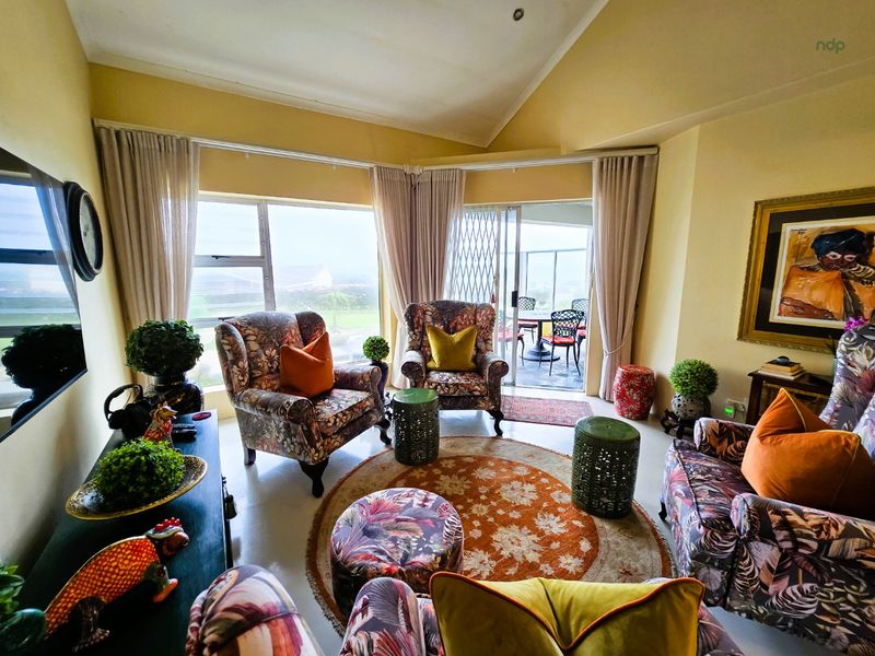 A bright living room featuring a vaulted ceiling, tiled flooring, and large sliding glass doors that provide access to an outdoor patio area.