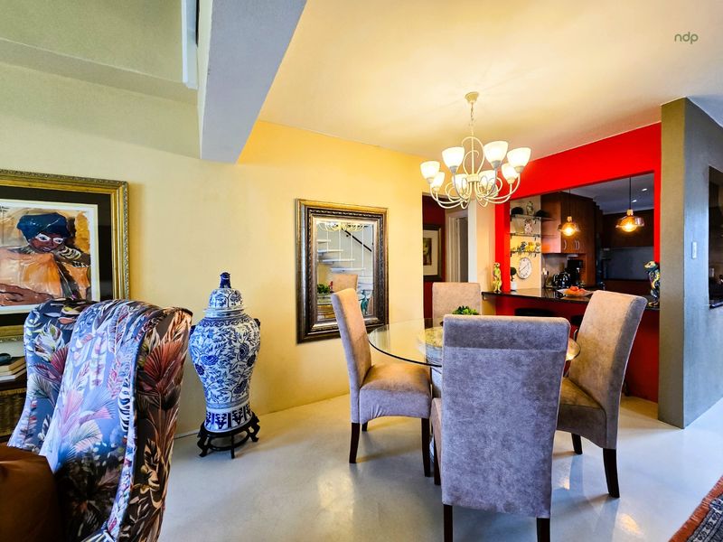 Open plan dining area featuring a central chandelier, adjacent breakfast bar, and views into the kitchen space with a staircase visible in the background.