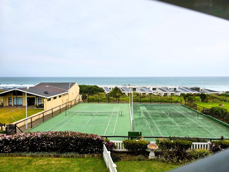 View of communal tennis courts within the estate, featuring well-maintained landscaping and proximity to the coastline.