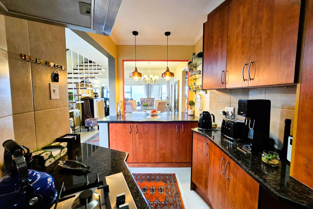 A functional kitchen featuring wooden cabinetry, granite countertops, a gas hob with extractor fan, and a tiled backsplash, opening into the dining area.
