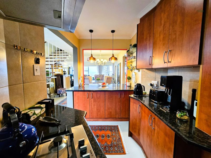 A functional kitchen featuring wooden cabinetry, granite countertops, a gas hob with extractor fan, and a tiled backsplash, opening into the dining area.
