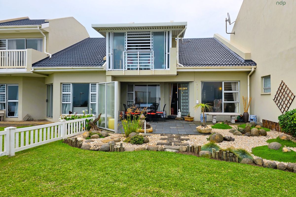 Rear view of the townhouse featuring a paved patio, landscaped garden with stone accents, a picket fence, and an upper-level balcony with sliding doors.