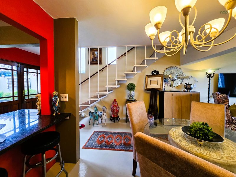Open plan living and dining area featuring a staircase, granite breakfast bar, and decorative chandelier, creating a connected and functional living space.
