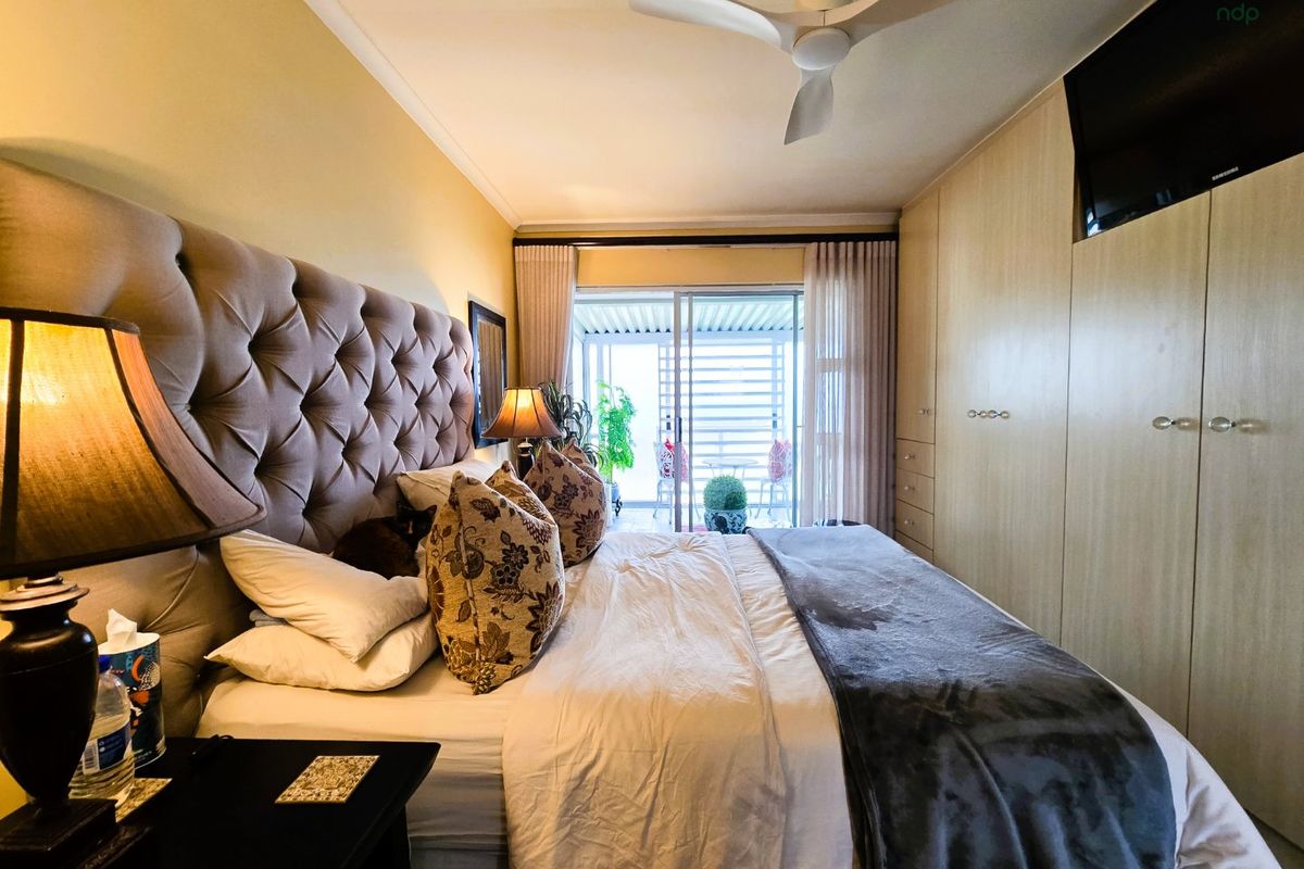 A well-maintained bedroom featuring built-in cupboards, a ceiling fan, and direct access to a private balcony through sliding glass doors.