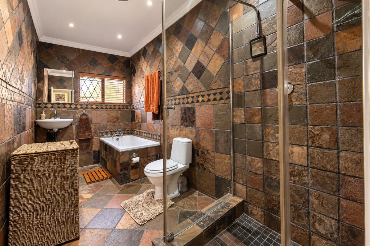 A full bathroom featuring a built-in bathtub, a separate glass-enclosed shower, a wall-mounted basin, and a toilet, finished with rustic stone-style wall and floor tiles.