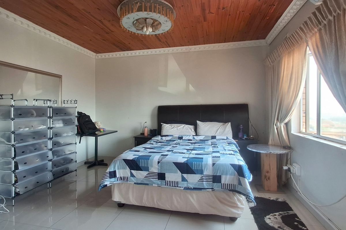 A bedroom featuring a timber-paneled ceiling with crown molding, tiled flooring, and a large window allowing natural light.