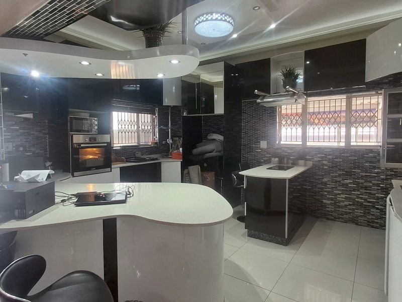 Modern kitchen featuring a unique curved island, glossy cabinetry, mosaic tile backsplash, built-in oven, and recessed ceiling lighting.