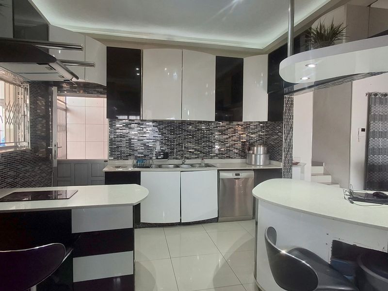 Modern kitchen featuring high-gloss cabinetry, a striking mosaic tile backsplash, integrated appliances, and a functional breakfast bar with recessed lighting.