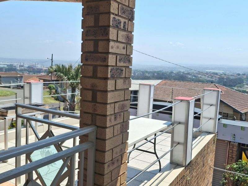 An elevated balcony featuring brick pillars, metal railings, and a built-in braai, offering expansive views of the surrounding neighborhood.