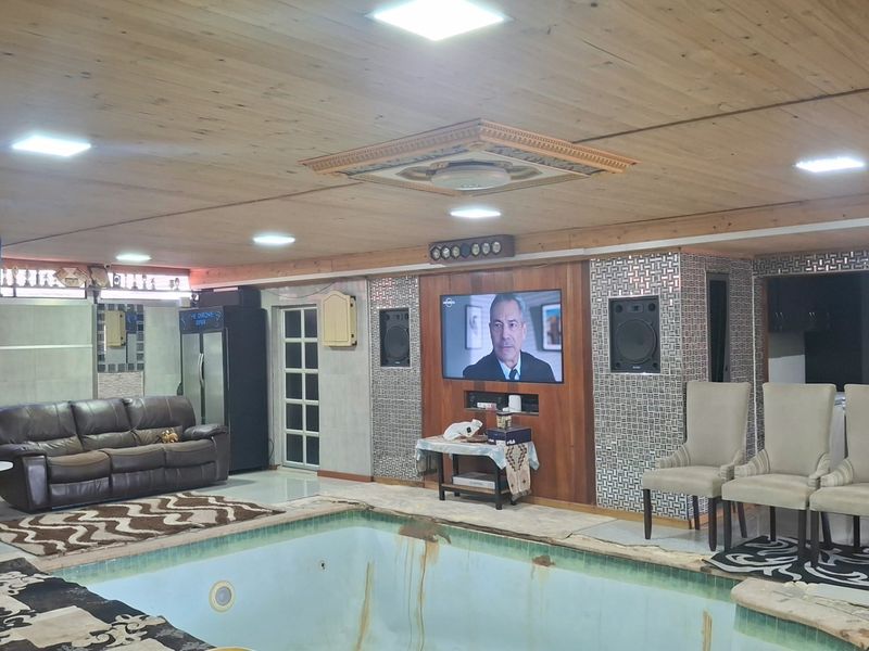 Indoor pool area featuring a wood-paneled ceiling, recessed lighting, and decorative wall tiling, currently integrated into a multi-purpose living space.