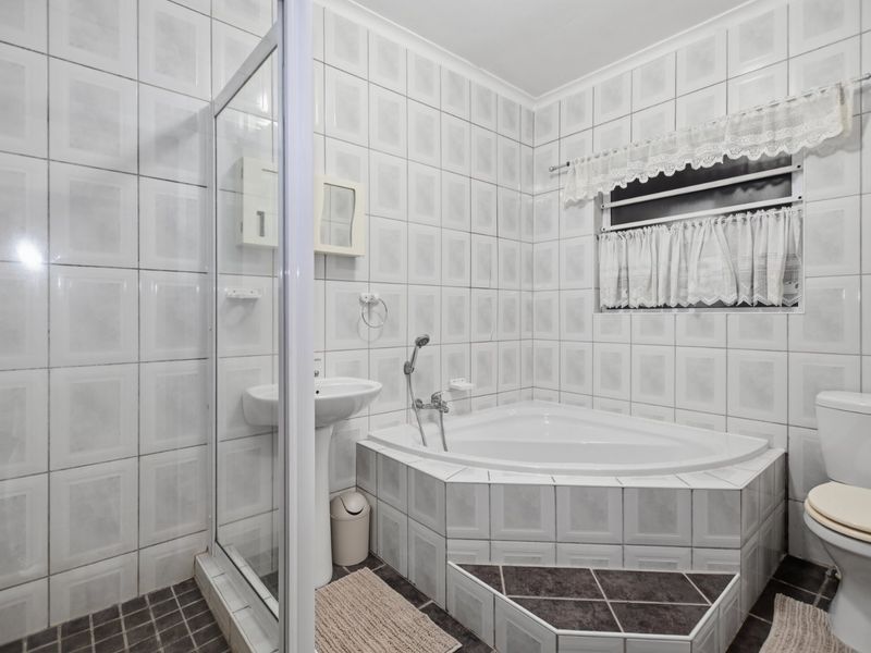 A functional bathroom featuring a corner bathtub, separate shower enclosure, pedestal basin, and toilet with neutral wall and floor tiling.