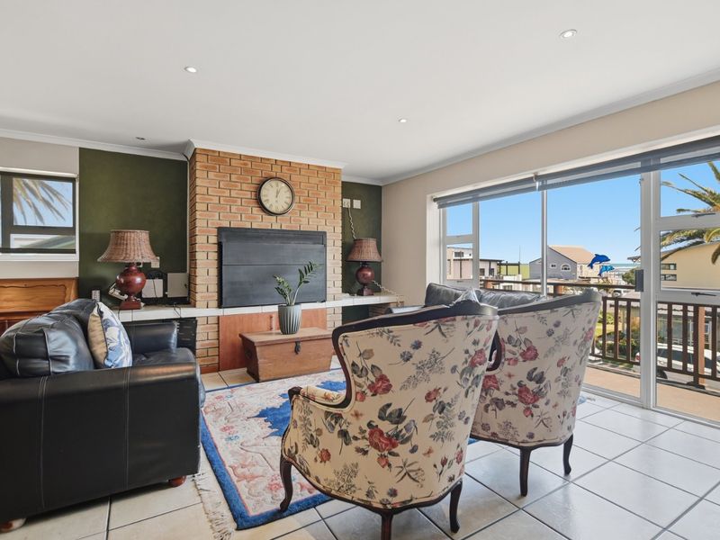 Spacious living room featuring a prominent brick fireplace, ceramic tiled flooring, and large sliding glass doors opening to an outdoor balcony with coastal views.