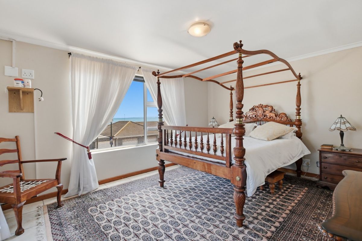 A spacious bedroom featuring tiled flooring, a ceiling light fixture, and a window with views of the surrounding area.