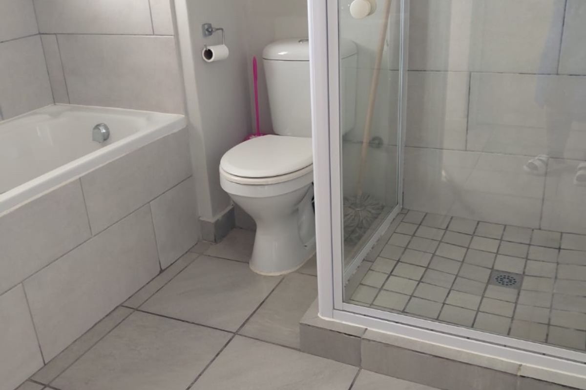 A functional bathroom featuring a built-in bathtub, a separate glass-enclosed shower, and neutral ceramic tiling throughout.