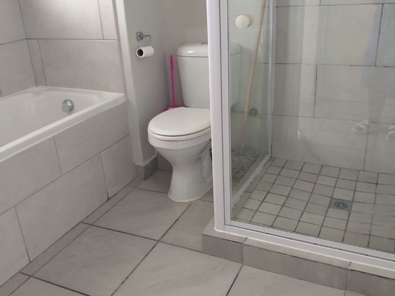 A functional bathroom featuring a built-in bathtub, a separate glass-enclosed shower, and neutral ceramic tiling throughout.