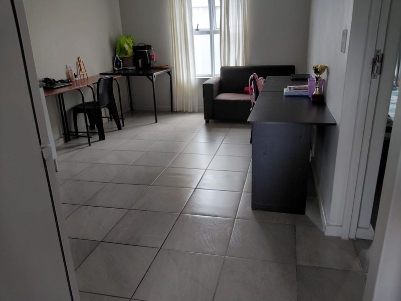 A functional living area featuring neutral tiled flooring and natural light from a window, offering a versatile space for various uses.