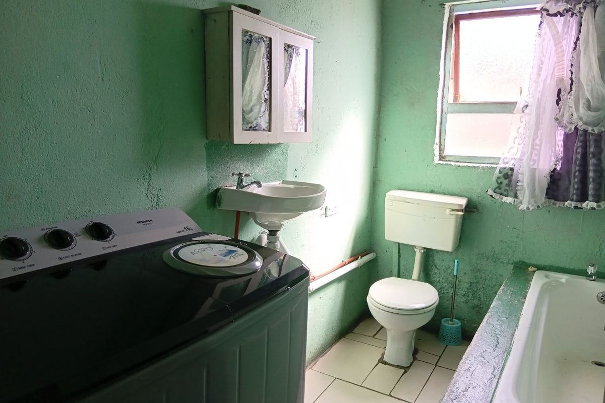 A functional bathroom featuring a built-in bathtub, toilet, and wall-mounted basin, requiring cosmetic updates to improve the overall condition and aesthetic appeal.