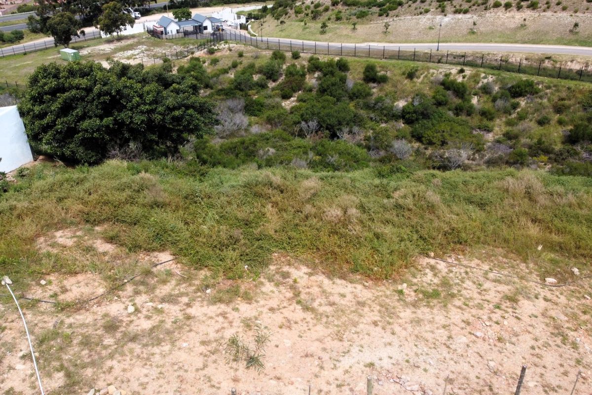 An aerial view of a vacant residential plot featuring sloped terrain and natural vegetation, bordered by perimeter fencing.