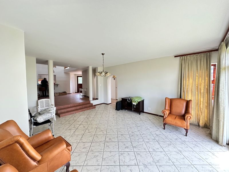 Spacious living area featuring tiled flooring, structural columns, and a raised platform leading to an adjacent space, offering a versatile open-plan layout.