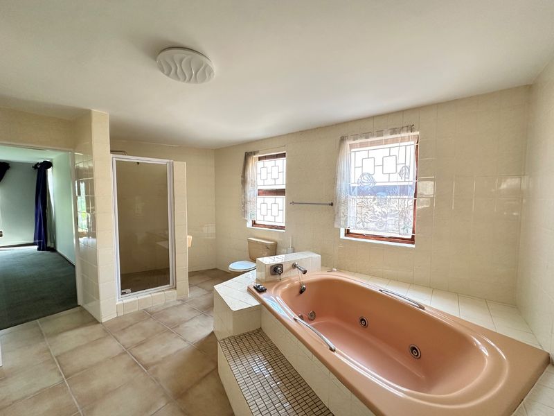 Spacious bathroom featuring a built-in bathtub, separate shower enclosure, and toilet, finished with neutral wall tiles and floor tiling.