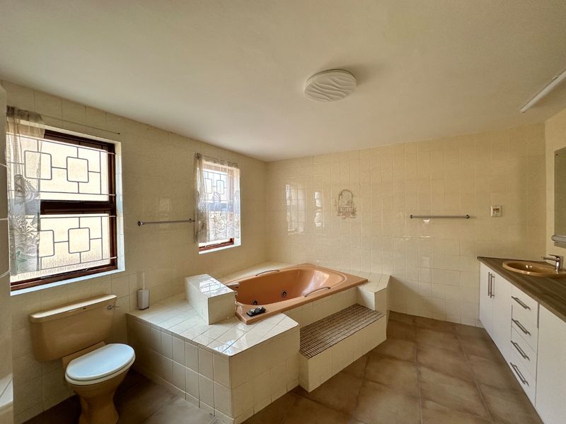 Spacious bathroom featuring a built-in bathtub, tiled vanity with storage cabinetry, and neutral wall and floor tiling.
